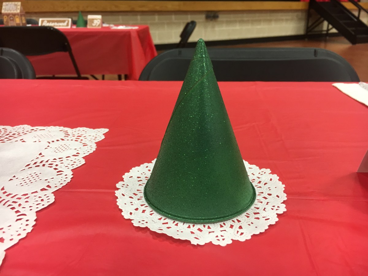 An upside down cone shaped cup painted to look like an evergreen tree, placed on a round doilies
