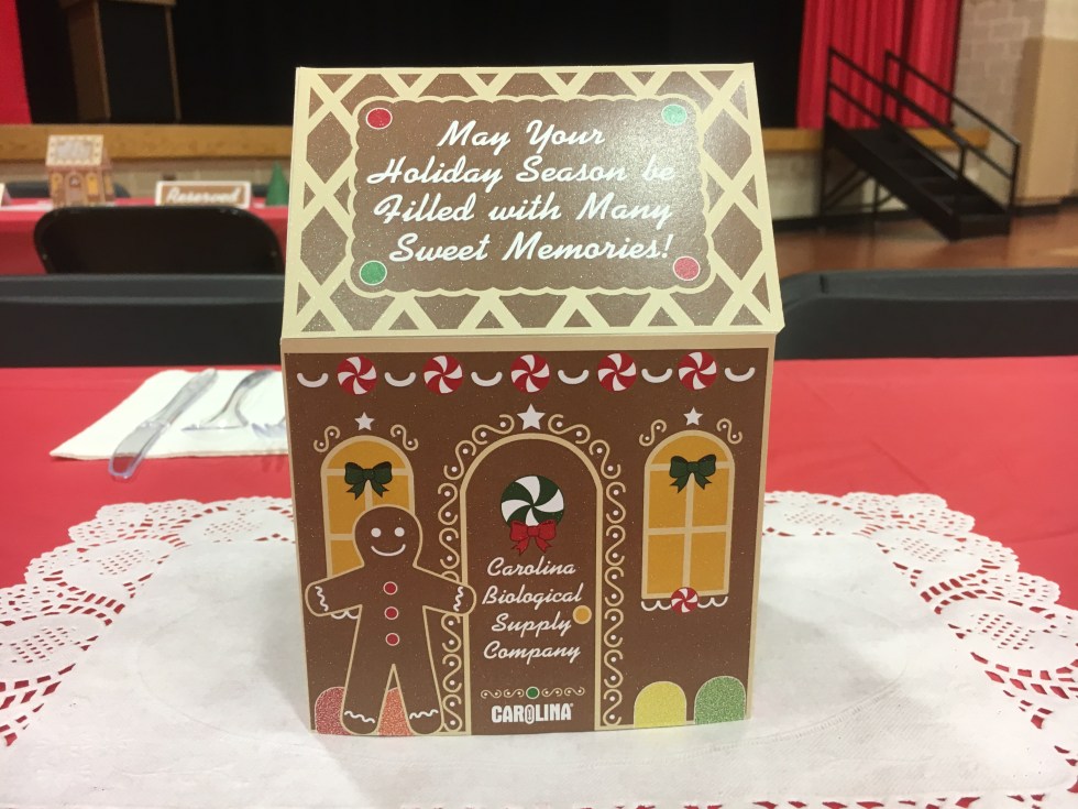 The front side of a paper gingerbread house, sitting on a doilie