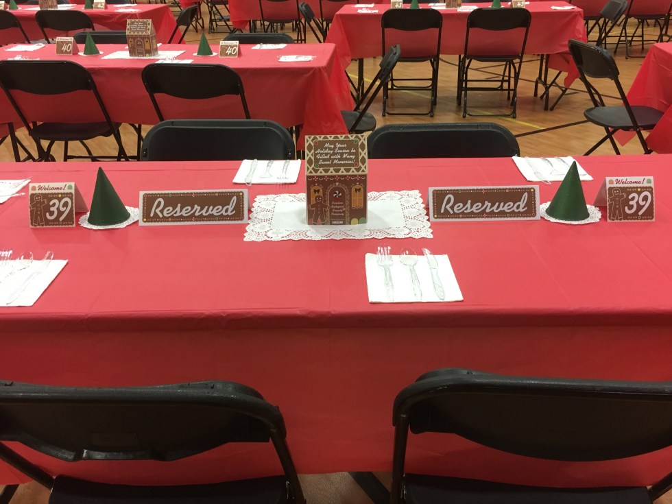 A table with table number tent cards, reserved tent cards, a paper gingerbread house with paper trees on either side